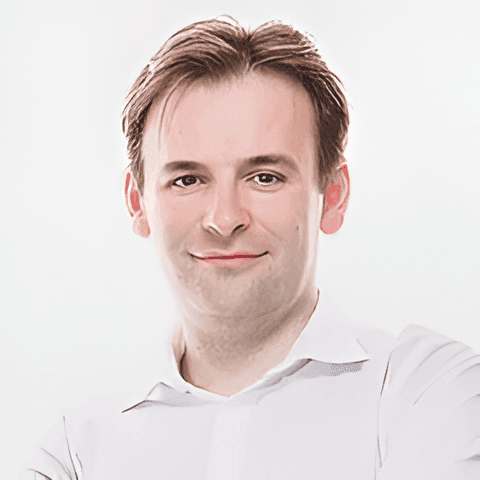 Person with short hair wearing a white collared shirt, standing against a plain white background.